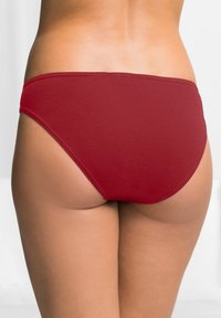 Bas de bikini rouge en tissu lisse et extensible avec une coupe taille basse et une couverture minimale. Bords sans couture pour une finition nette.