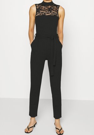Schwarzer Jumpsuit mit Spitzen-Ausschnitt, ärmellosem Design, schmal zulaufenden Beinen und Taillenknoten. Hergestellt aus glattem Stoff mit klassischer Passform.