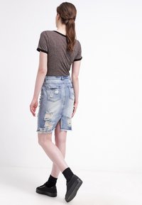 Jeanskjol med slitna detaljer, ljusblå färg, midilängd, fransad byxkant och bakfickor. Matchad med en grå topp och svarta skor.