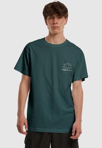 Mørkeblå bomulds T-shirt med rund halsudskæring, korte ærmer og et hvidt lotus logo på venstre bryst. Glat tekstur, afslappet pasform.
