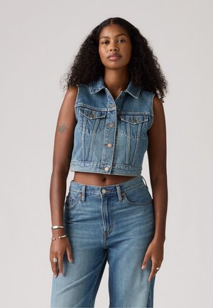 Lichtblauwe denim cropped vest met mouwloos ontwerp, vooraan knopen en twee borstzakken. Gecombineerd met hoge taille bijpassende jeans.