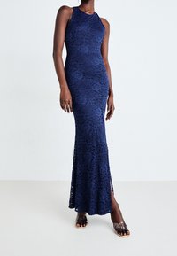 Abito maxi blu navy in pizzo con motivi floreali, design senza maniche e spacchi laterali. Texture liscia con silhouette aderente.