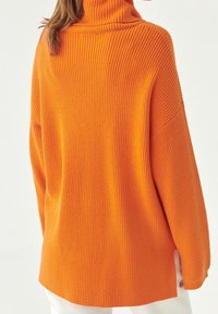 Yliön turtleneck-neule kirkkaan oranssista ribbitettystä kankaasta, jossa on lievästi pudotetut olkapäät ja sivurei'ät helmassa.