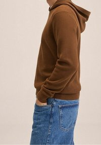 Bruine kaptrui gemaakt van gestructureerde stof, met een ribbelontwerp en een kangoeroezak, gecombineerd met denim jeans.