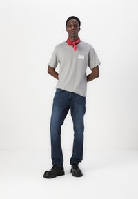 Gray short-sleeve t-shirt with white logo, paired with blue jeans and black chunky boots. A red bandana is worn around the neck.
