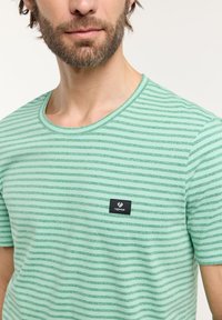 Groene gestreepte t-shirt met ronde hals, korte mouwen en een klein zwart logo label op de linkerborst.