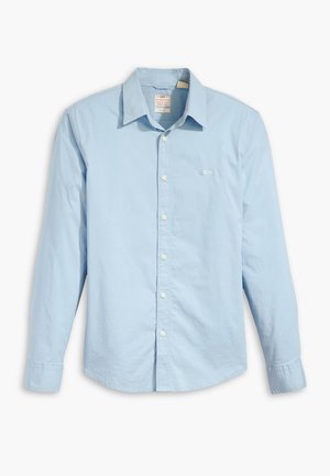 Chemise boutonnée à manches longues bleu clair en coton, avec un col classique, des boutons blancs et un petit logo sur la poitrine gauche.