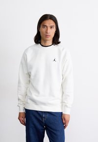 Hvid sweatshirt lavet af blødt stof, med rund halsudskæring og ribbede manchetter. Et lille sort Jordan-logo er broderet på brystet.