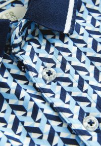 Polo shirt blu con motivo geometrico, caratterizzato da colletto blu navy e dettagli bianchi. Dettaglio dei bottoni visibile sulla patta. Materiale in cotone.
