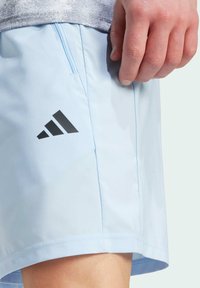 Svetlomodré športové šortky vyrobené z hladkej textílie, s vreckom na zips a čiernym logom na boku.