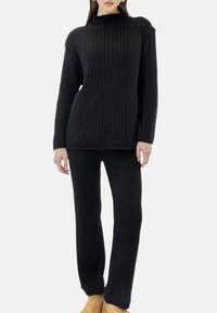 Sort strikket outfit med ribbet tekstur, højhalset sweater og matchende ribbede bukser med let flare ved anklerne.