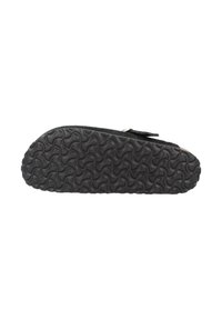 Semelle de sandale noire avec un motif de grip texturé et ondulé visible sur le dessous, montrant une partie de la sangle et de la boucle.