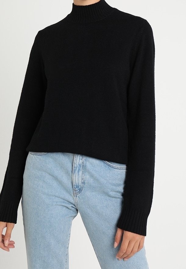 Zwarte coltrui van zachte stof met lange mouwen en geribbelde manchetten, gecombineerd met lichtblauwe jeans.