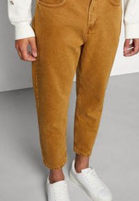 Pantaloni corduroy bej cu un design drept, având buzunare frontale și o textură subtilă, asortați cu adidași albi.