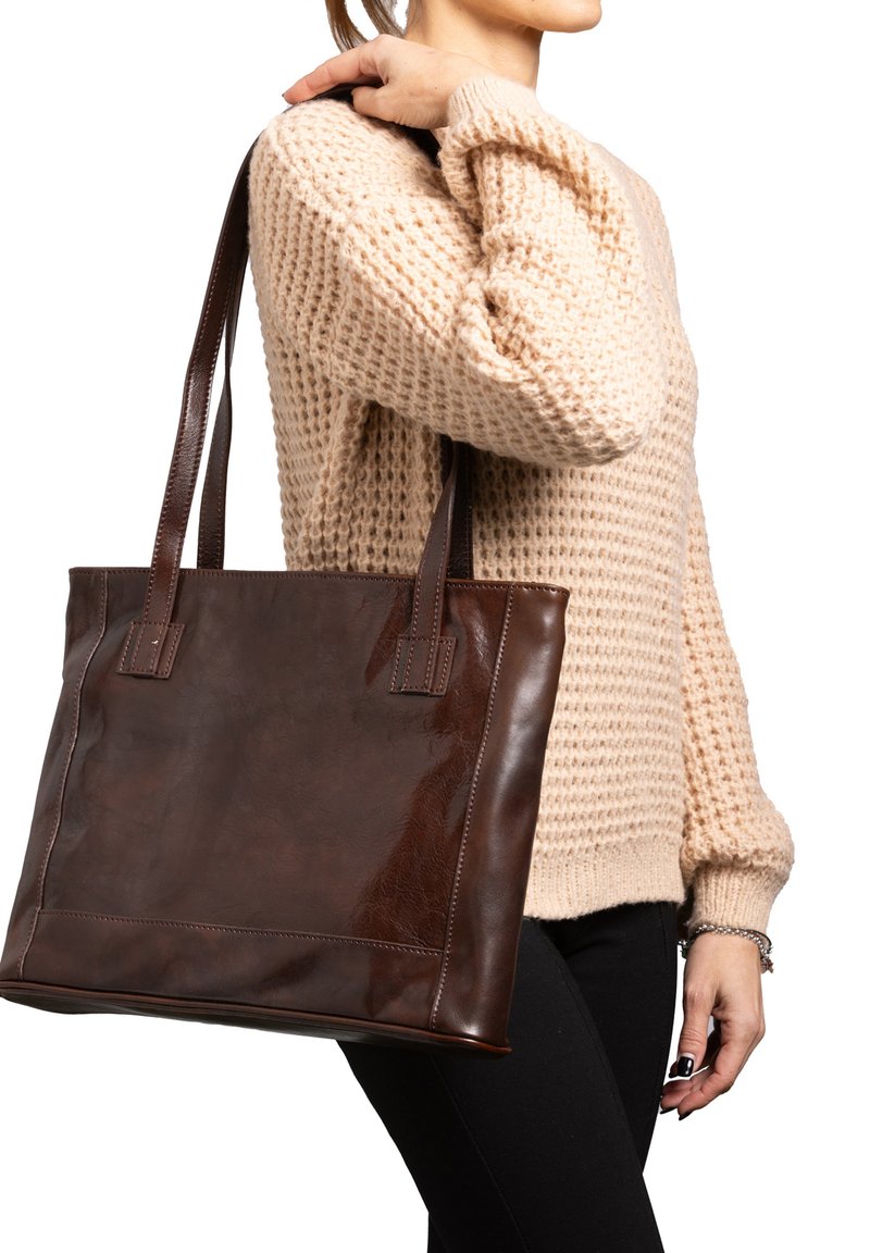 Borsa tote in pelle marrone con texture liscia, forma rettangolare e manici doppi. Indossata sopra un maglione beige con un motivo lavorato a maglia.
