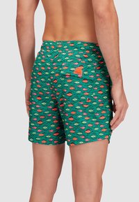 Pantaloni da bagno in tessuto verde con un motivo di pesci in rosa e arancione. Vita elastica con una tasca sul retro e un piccolo dettaglio del logo.