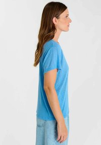 Kortärmelig blauw T-shirt met een ronde hals. Gemaakt van zachte stof, heeft een ontspannen pasvorm en een zachte textuur. Gecombineerd met lichte spijkerbroek.