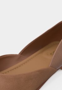 Gros plan sur une chaussure plate en daim marron avec semelle intérieure rembourrée et bride élastique autour du talon.