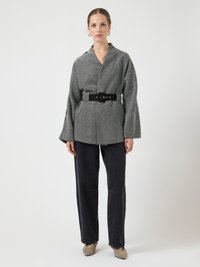 Blazer gris con estampado y mangas anchas, ceñido en la cintura con un cinturón negro. Combinado con vaqueros oscuros y tacones gris claro.