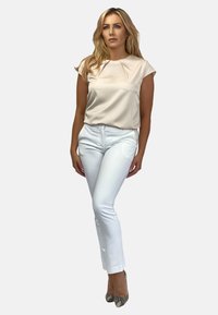 Kremowa satynowa bluzka z krótkimi rękawkami, połączona z dopasowanymi białymi spodniami i butami na obcasie we wzór węża. Elegancki, dopasowany wygląd.