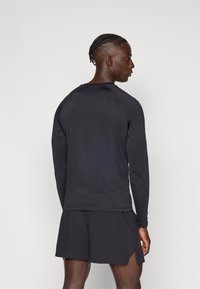 Melna garām piedurknēm sporta krekls ar apaļu kaklu un raglāna piedurknēm, kopā ar melnām šortām ar sānu šķērēm ventilācijai.