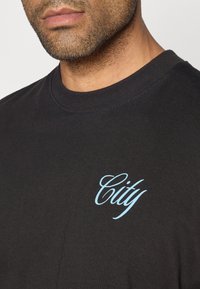 Čierne bavlnené tričko s klasickým okrúhlym výstrihom, na hrudi s nápisom "City" v svetlomodrom kurzívnom písmene, s hladkou textúrou.