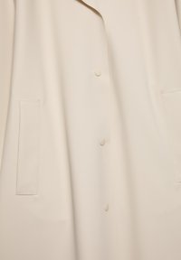 Végezett be a zöld kabát, amely sima anyagból készült, füles gallérral, két elülső zsebbel és három gombbal a fronthoz.