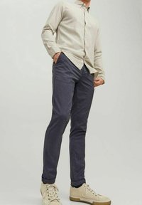 Vaaleanbeige nappipaita yhdistetty tummansinihin slim-fit-housuihin ja vaaleanbeigeihin kengissä, joissa on tekstuurinen pinta ja kumipohja.