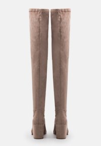 Un paio di stivali alti in suede taupe con tacco a blocco, visti da dietro su uno sfondo bianco.