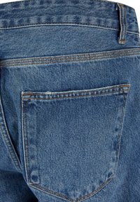 Jeans de mezclilla azul con un bolsillo trasero reforzado y costuras en contraste de color naranja. La tela tiene una textura suave y un ligero desgaste.