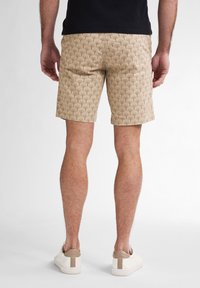 Pantaloncini beige a fantasia con un motivo a foglia ripetuto, realizzati in tessuto leggero, abbinati a scarpe bianche slip-on con un accento taupe sul retro.