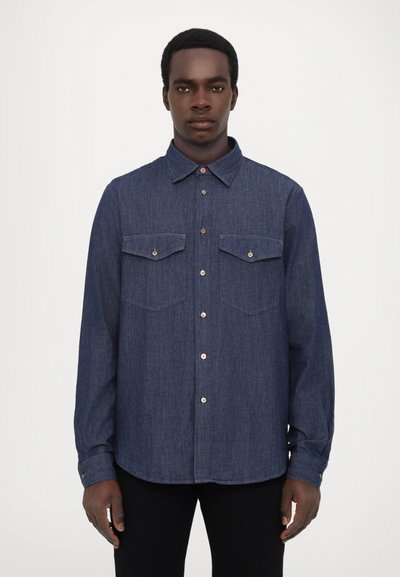Chemise en denim à manches longues de couleur bleu foncé avec un col boutonné, deux poches avant et des accents métalliques. Texture lisse avec une coupe ajustée.