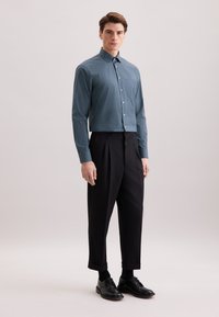 Camicia blu a motivo con colletto classico, chiusura con bottoni sul davanti e maniche lunghe abbinata a pantaloni neri a vita alta e scarpe eleganti nere.