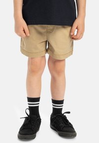 Khaki shorts med rullade kantar, bärs med svarta sneakers och svarta strumpor med två vita ränder. Slät tyg, enkel design.