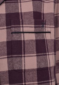 Plaid shirt featuring shades of dark purple and light pink, textured fabric, with a left chest pocket outlined in black.