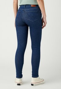 Ciemnoniebieskie dopasowane dżinsy o gładkiej fakturze denimu, z skórzaną naszywką w talii oraz dwoma tylnymi kieszeniami z delikatnym przeszyciem.