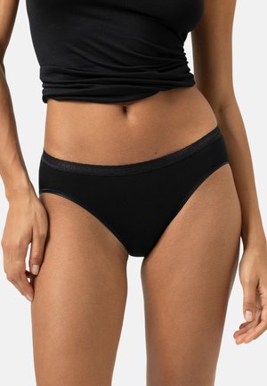 Woman wearing black high-cut underwear and black cropped tank top, shown from midriff to upper thighs on white background.