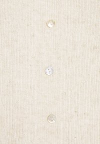 Cardigan de punto acanalado beige claro con cuatro botones transparentes en la parte frontal. La textura es suave con un sutil patrón vertical.