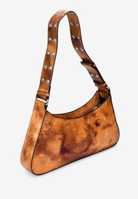 Bolso de hombro de cuero marrón con forma curvada, acabado texturizado y acentos de tiras con tachuelas. Presenta un borde negro a lo largo de las costuras.