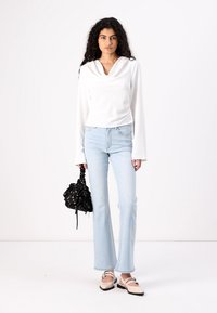 Haut à col roulé blanc à manches longues, jean évasé bleu clair, sac à main noir à motifs et ballerines beige avec un détail de bride.