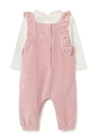 Romper per bambino in corduroy rosa con spalline arricciate, indossato sopra una maglietta bianca a maniche lunghe con chiusura a bottoni al collo.
