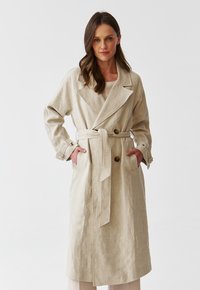 Beige linen trench coat with a tailored fit, large lapels, a tied waist, and buttoned pockets. Smooth texture, mid-length design.