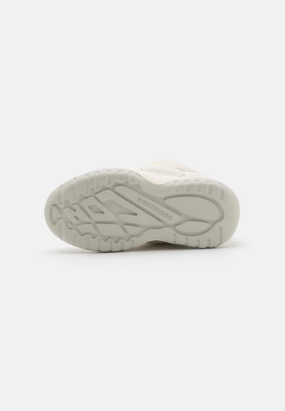 Shoe sole in off-white rubber with textured grip patterns and a raised logo. Features a rounded shape with side indentations.