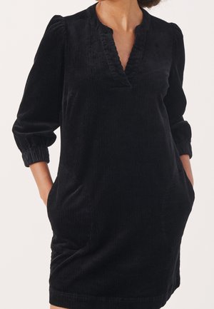 Black corduroy dress with a v-neck, long puff sleeves, and side pockets. Features subtle ribbed texture and a relaxed fit.