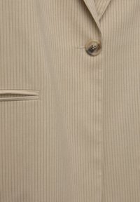 Beige pinstripe blazer fabric with a smooth texture, featuring a single brown button and a subtle, vertical stripe pattern.