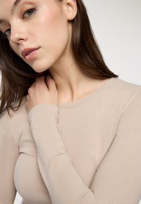 Beżowa bluzka z długim rękawem wykonana z prążkowanej tkaniny. Dekolt jest okrągły, a rękawy dobrze dopasowane, eksponujące gładką teksturę.