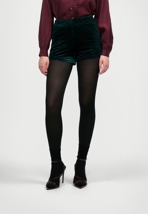Flonkerde groene hoge taille shorts met stippen, gecombineerd met zwarte opaque tights en open teen hoge hakken. Donker bordeaux lange mouwen blouse.