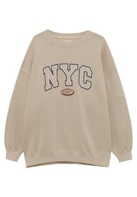Sweat-shirt beige col rond avec "NYC" en grandes lettres blanches et noires et un petit logo ovale sous le texte.