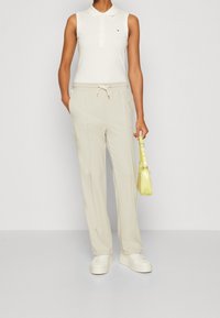 Valkoiset hihattomat polo-paidat, beige naruhousut, valkoiset lenkkarit ja pieni keltainen käsilaukku. Pehmeä kangas, rento istuvuus ja minimaalinen muotoilu.