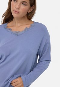 Top de manga larga morado claro con escote en V que presenta un intrincado borde de encaje. Textura suave y corte relajado, adecuado para el uso casual.